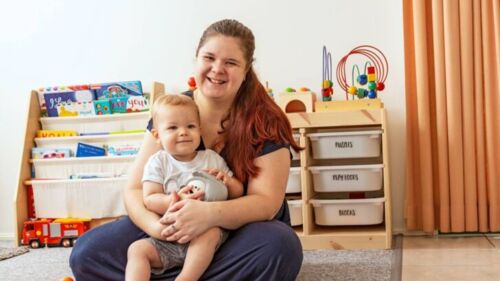 Woman and her child sit in play room, happy as they work towards financial independence.
