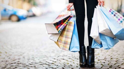 Person standing with shopping bags, representing how Australians are spending more on discretionary items post-pandemic.