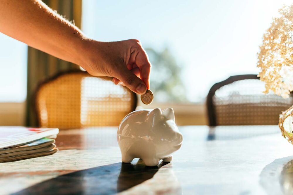 Man placing a coin into a piggy bank, symbolising saving and alternative investment strategies