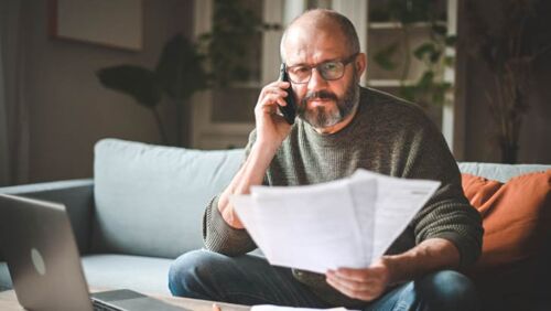 Australian retiree on a phone call with a superannuation fund while reviewing retirement and super paperwork at home.