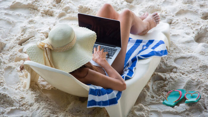 a woman works on the beach after boss forces her to take annual leave
