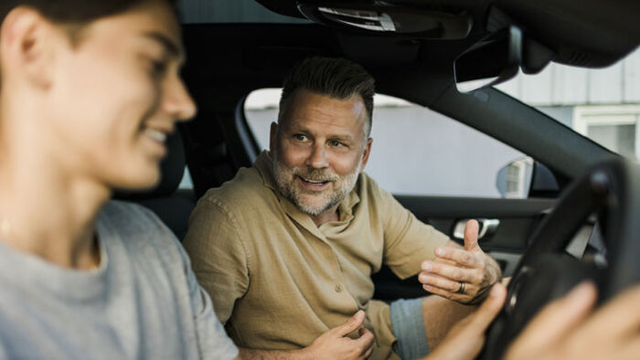 Father and adult son discussing a used car at a dealership before negotiating a purchase.