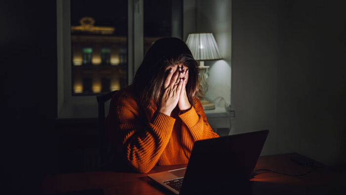 A worried woman reviewing bills on her laptop at the kitchen table.