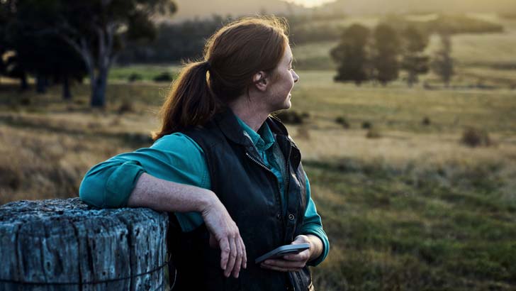 an australian farmer accesses her banking app while overlooking her farm in regional australia