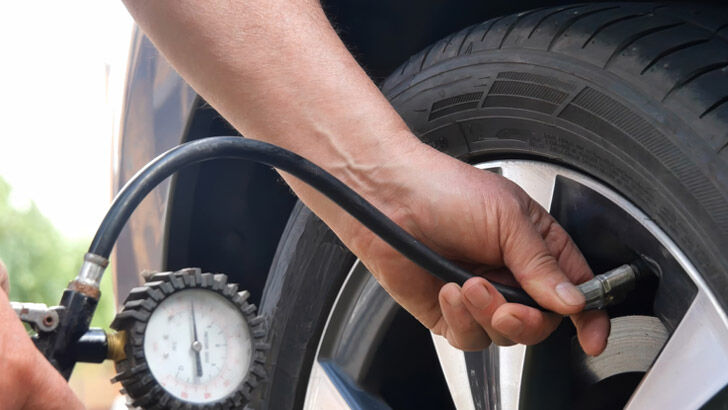 Driver checking tyre pressure before a road trip.