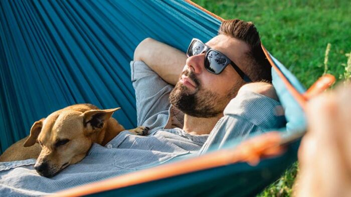 Relaxed man in a hammock with his dog, illustrating the benefits of doing less.