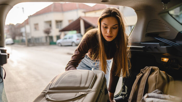 Woman loading luggage into a car before setting off on a road trip.